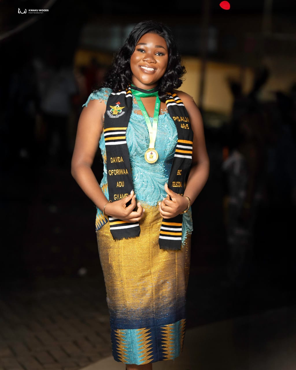 A graduate wearing the Golden Contrast sash and a medal, embroidered with her name, her degree and a crest.